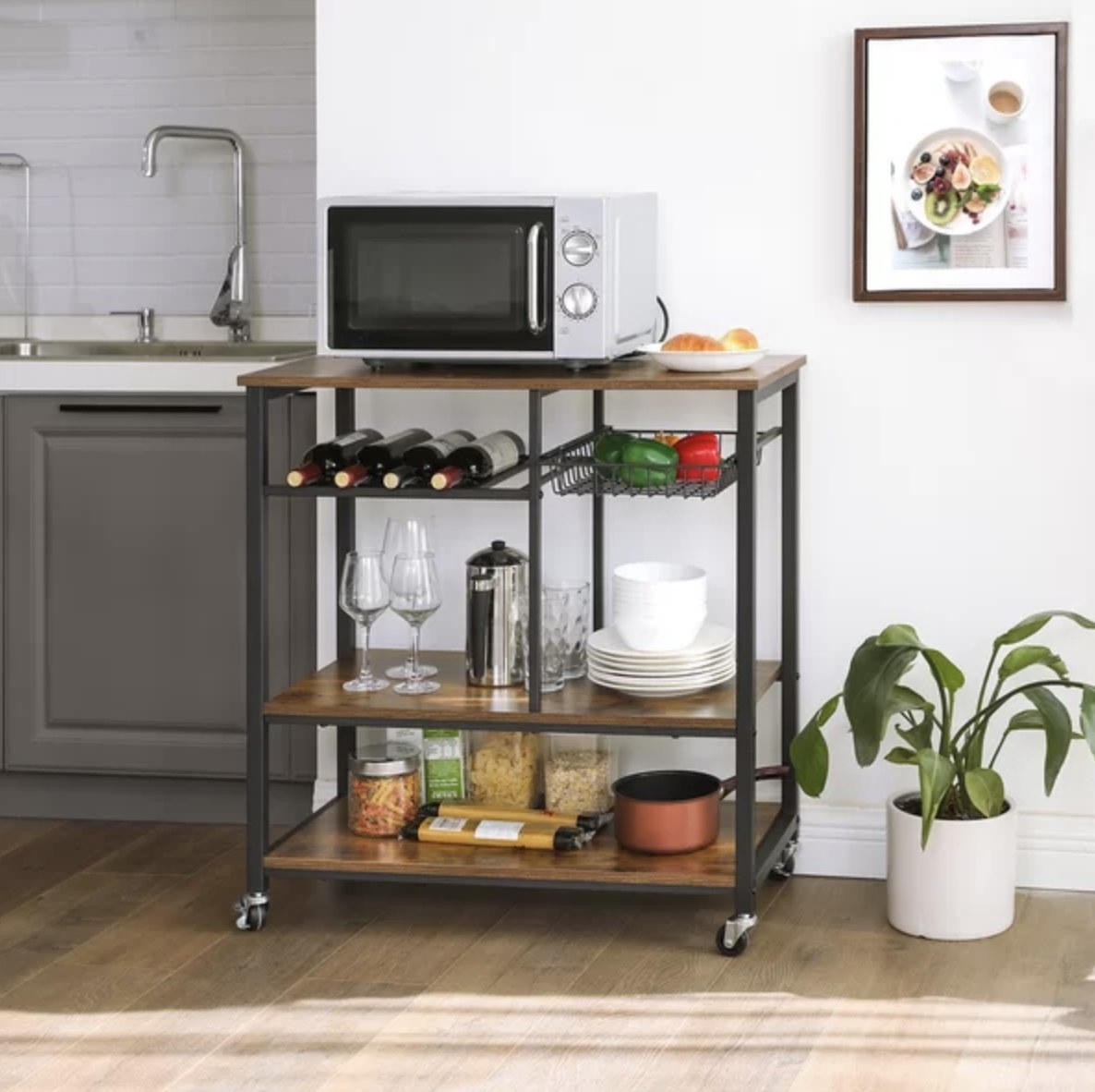 The black and wooden cart has a microwave, wine, serving ware and pasta supplies
