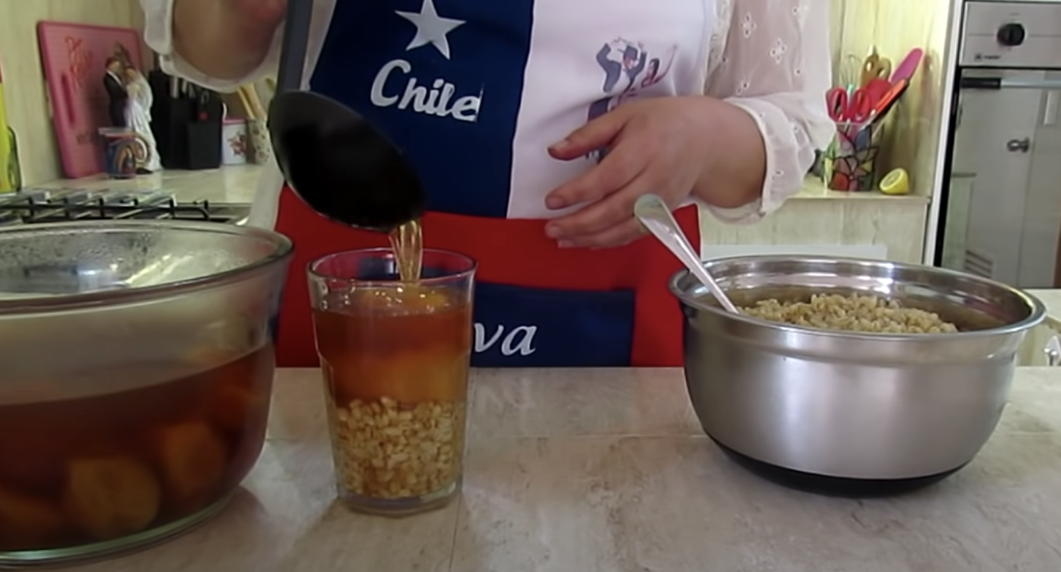 A person wearing a Chile shirt stands at a counter preparing mote con huesillos