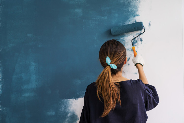 A woman painting her white wall blue.