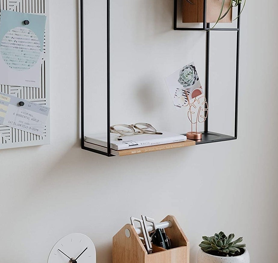 The shelf mounted on a wall with books, glasses, and accessories on it