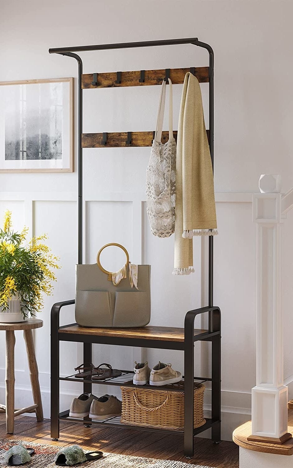 The coat rack with shoes, a tote bag, and some scarves hanging from it, next to an accent table with a plant on it