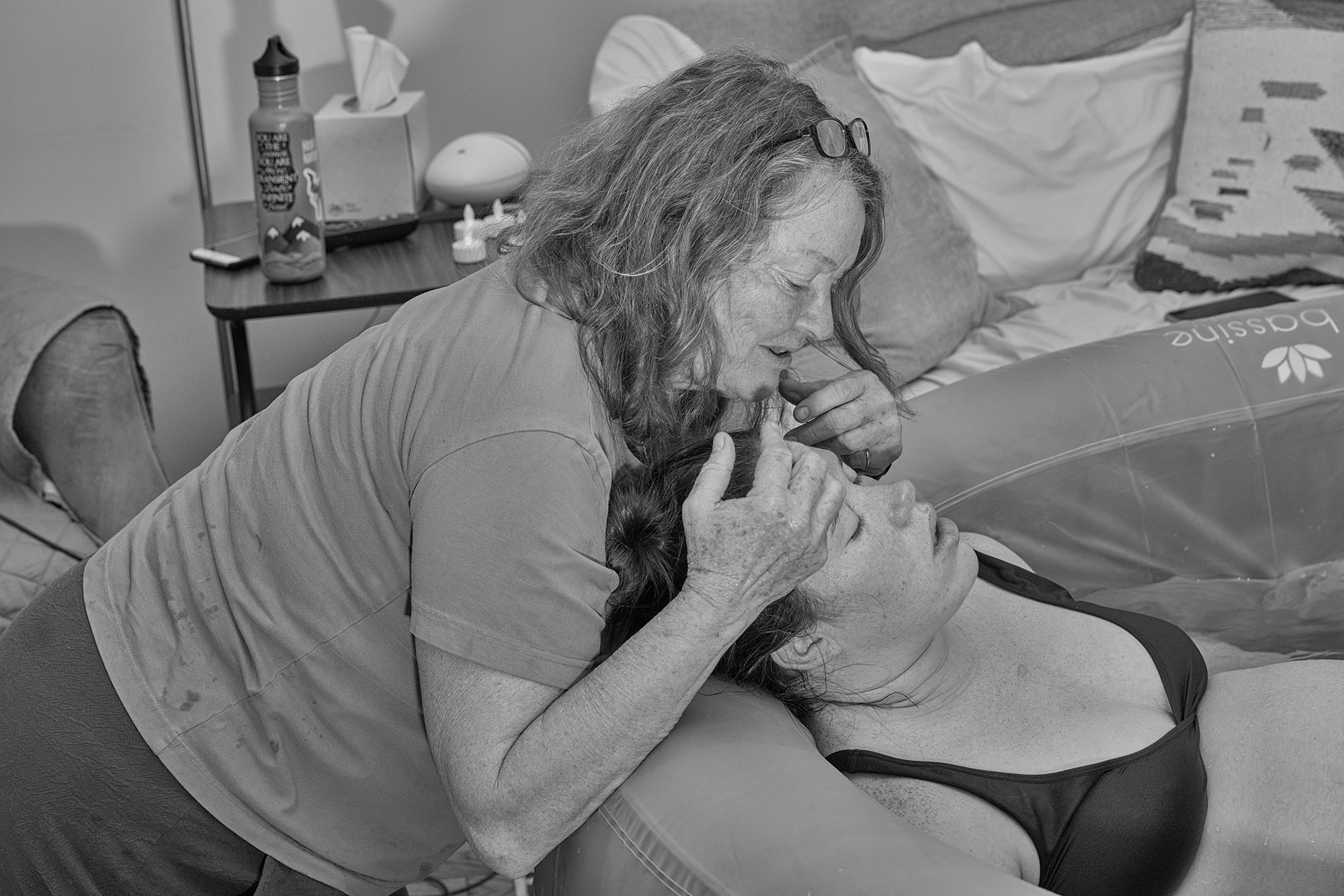 A woman is consoled in a birth tub by a midwife 