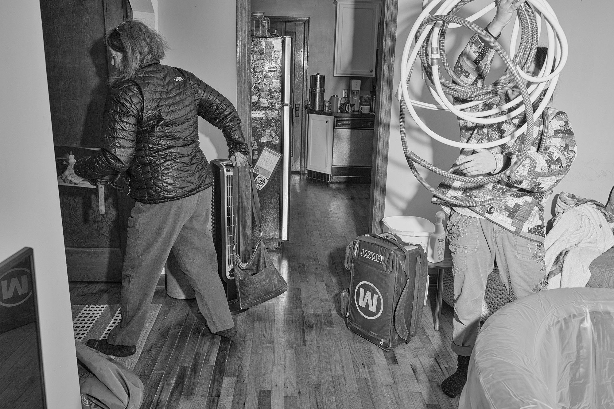 A woman carrying a purse and a man carrying a hose leave a house