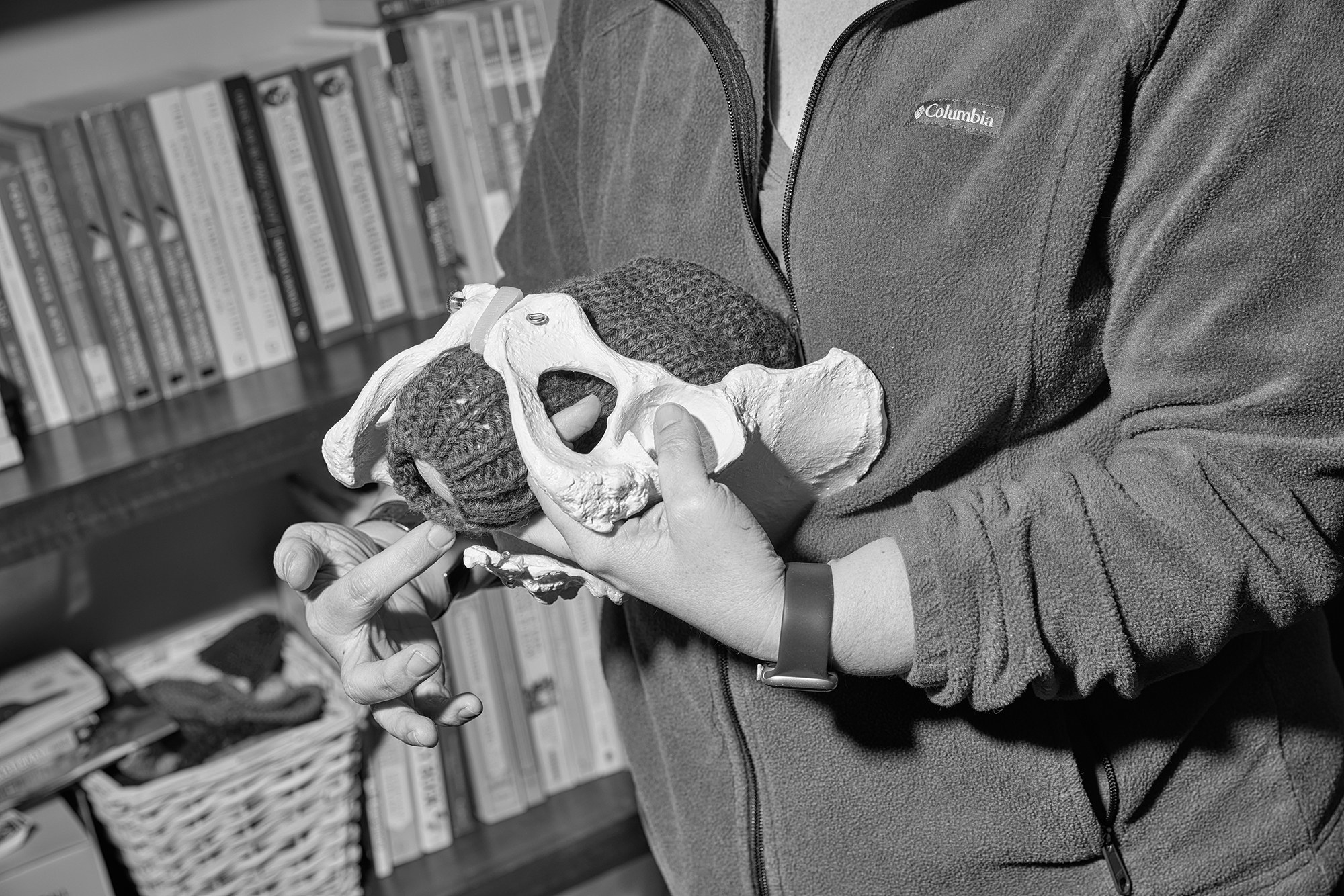 A woman holds a model with a pelvis and a knit hat to represent birth