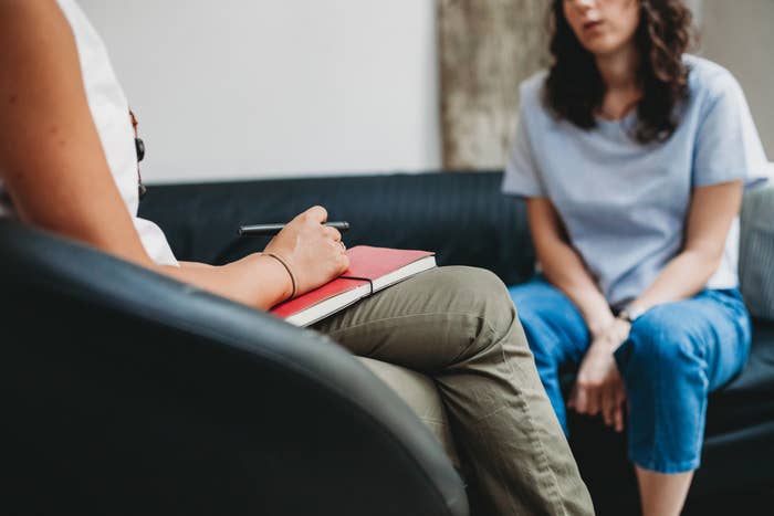 A woman sits on a couch across from a therapist during a session