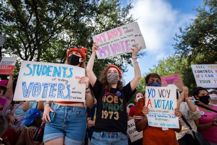 People wearing masks hold up various signs, including &quot;My Body My Choice My Vote My Voice&quot; and &quot;Students of Today Voters of Tomorrow&quot;