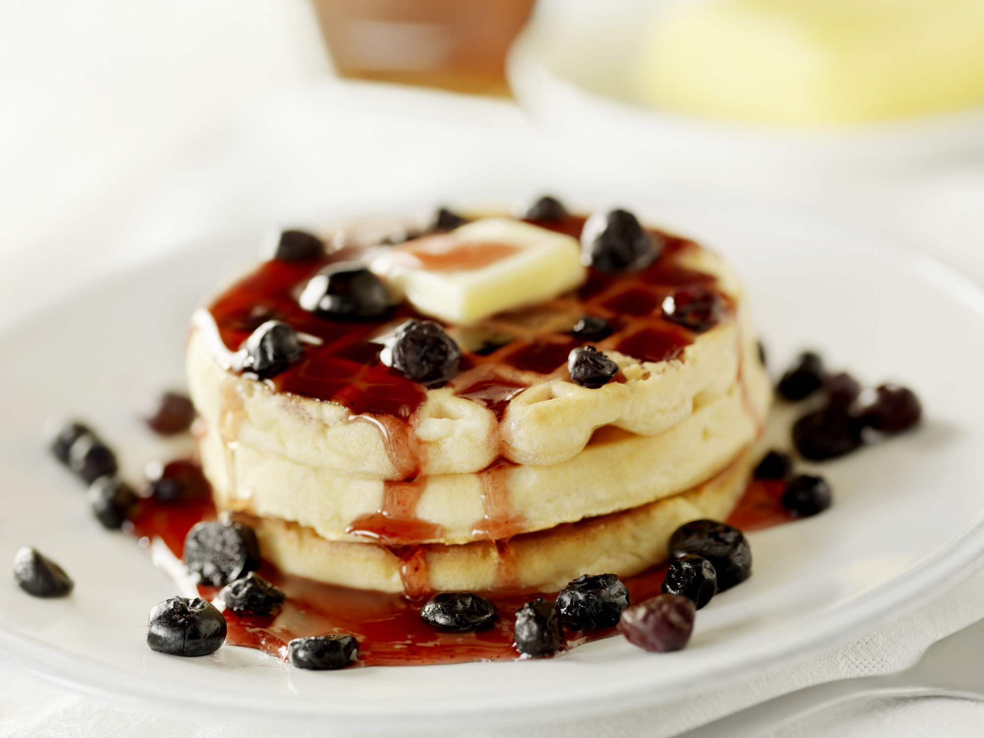 A stack of three waffles with reddish blueberry syrup and blueberries