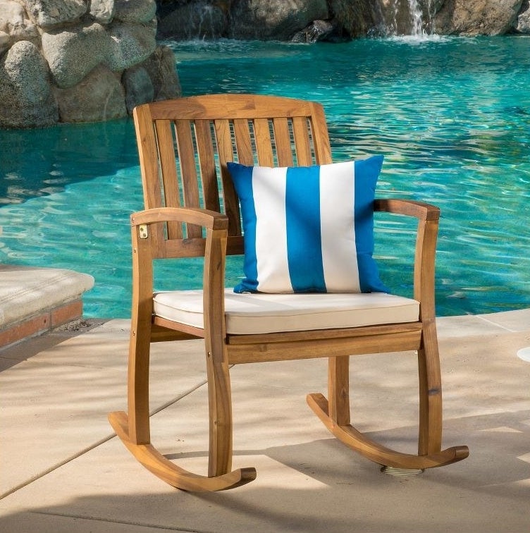 the rocking chair with white cushion and blue and white pillow on a pool deck