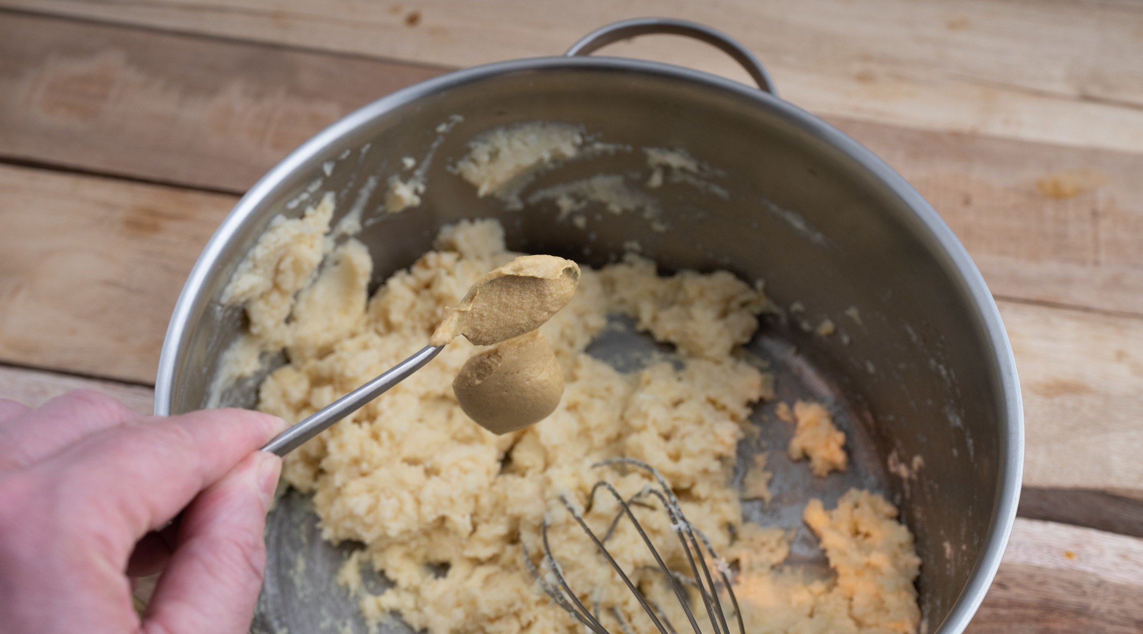 Pouring a scoop of mustard into a pot of mashed potatoes