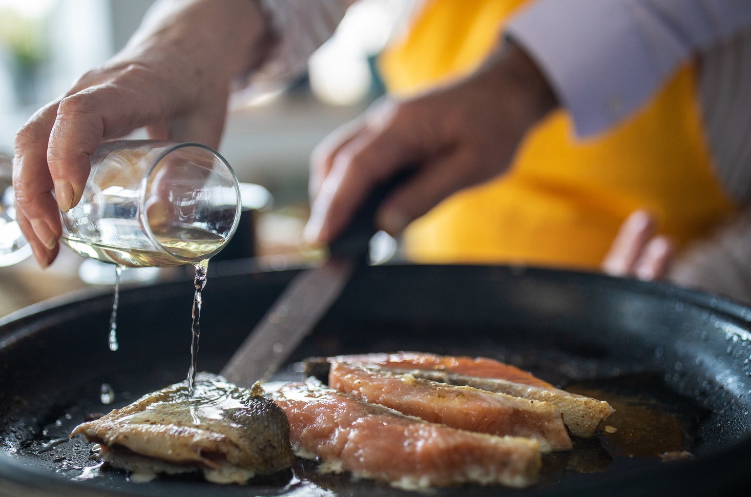 A woman adding white wine while preparing fish