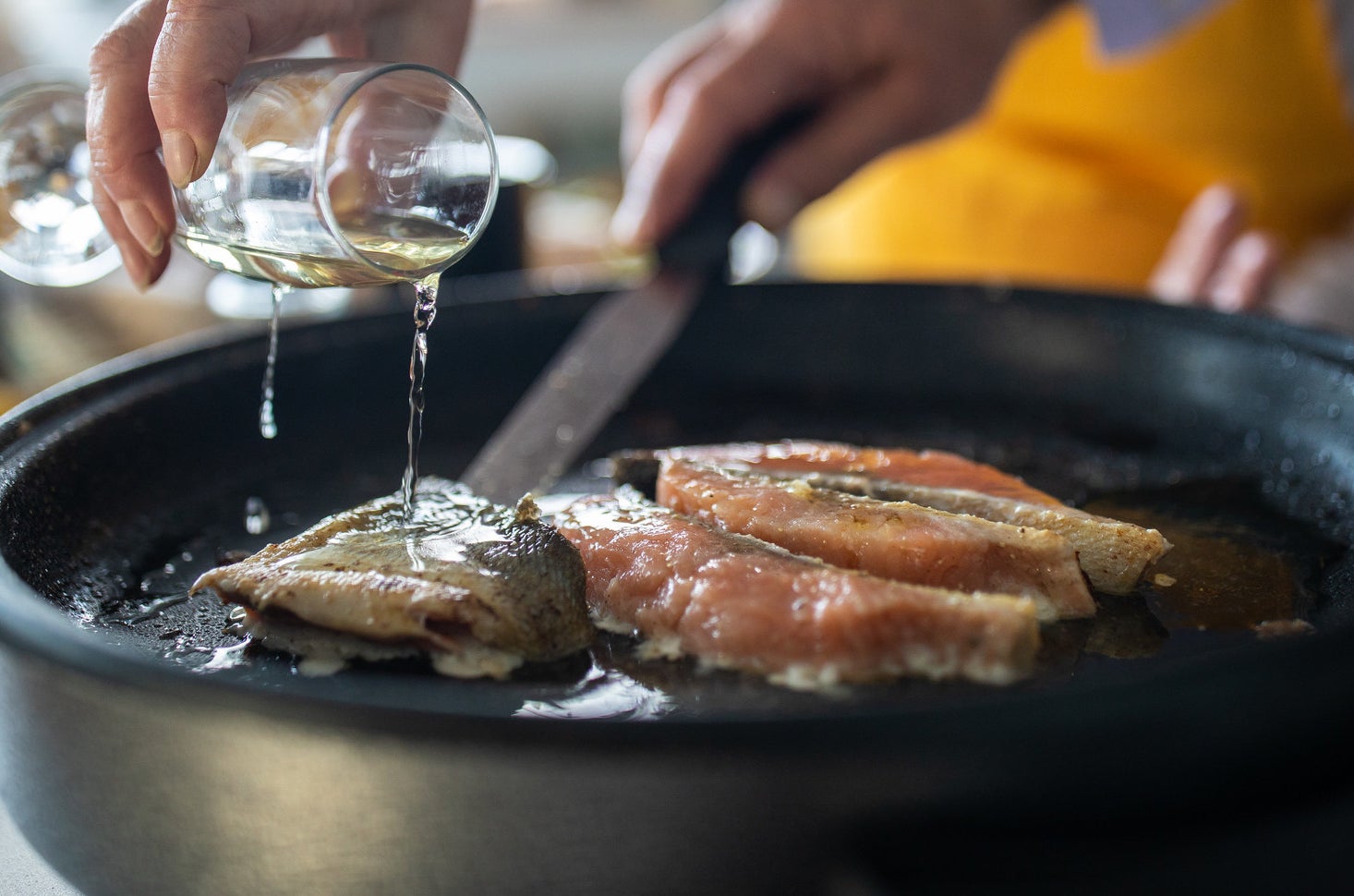 A woman adding white wine while preparing fish