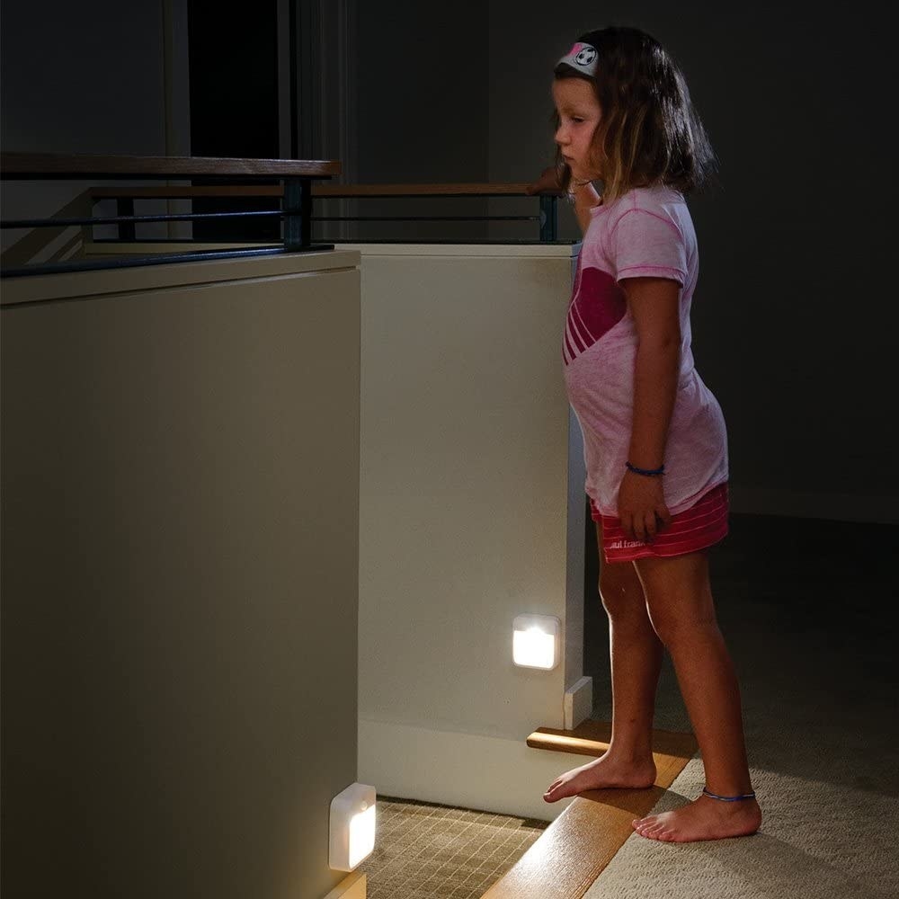 A child at the top of a staircase with two night lights on the walls