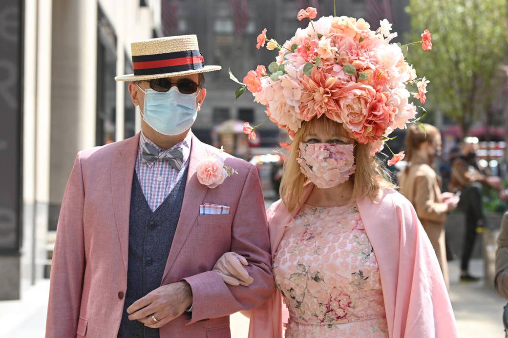 A woman wearing a lage floral arrangement and a man in a matching suit