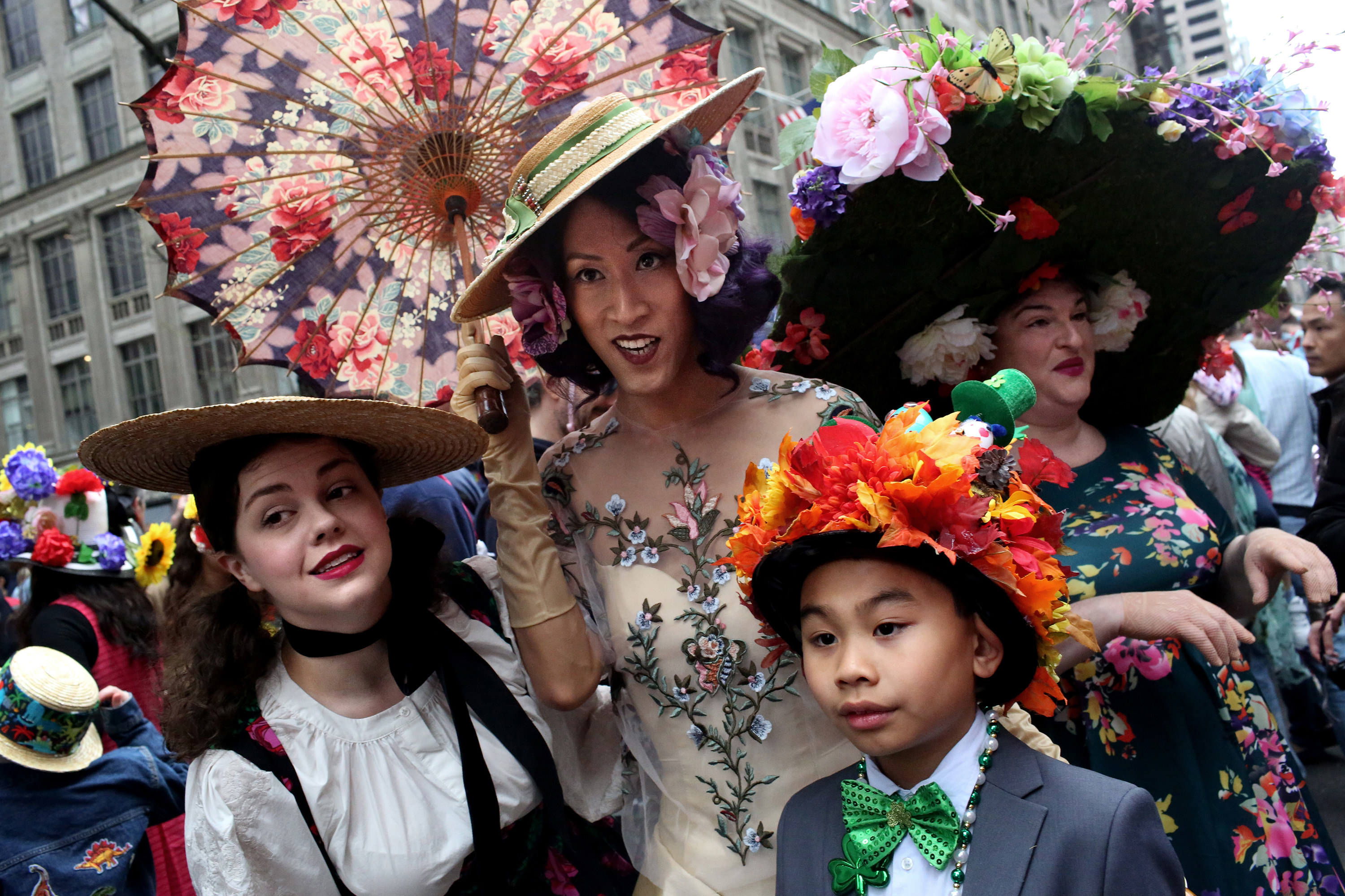 Four women with hats and elaborate costumes pose in the street 