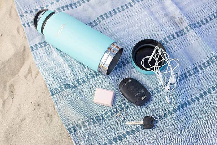 A water bottle on a blanket with a pair of headphones keys beside it