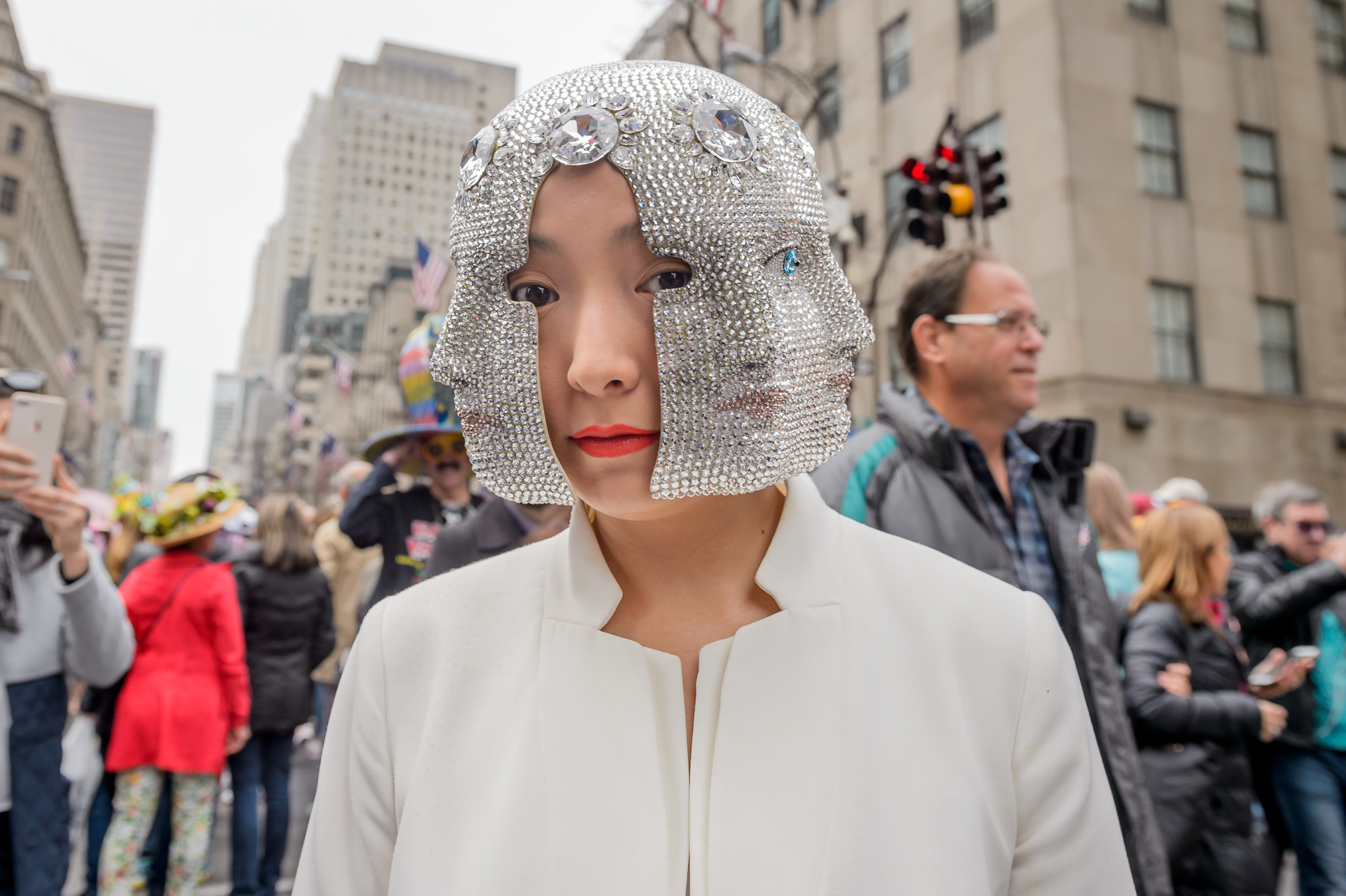A woman wearing a silver embellished mask stands amid a crowd of people on the street