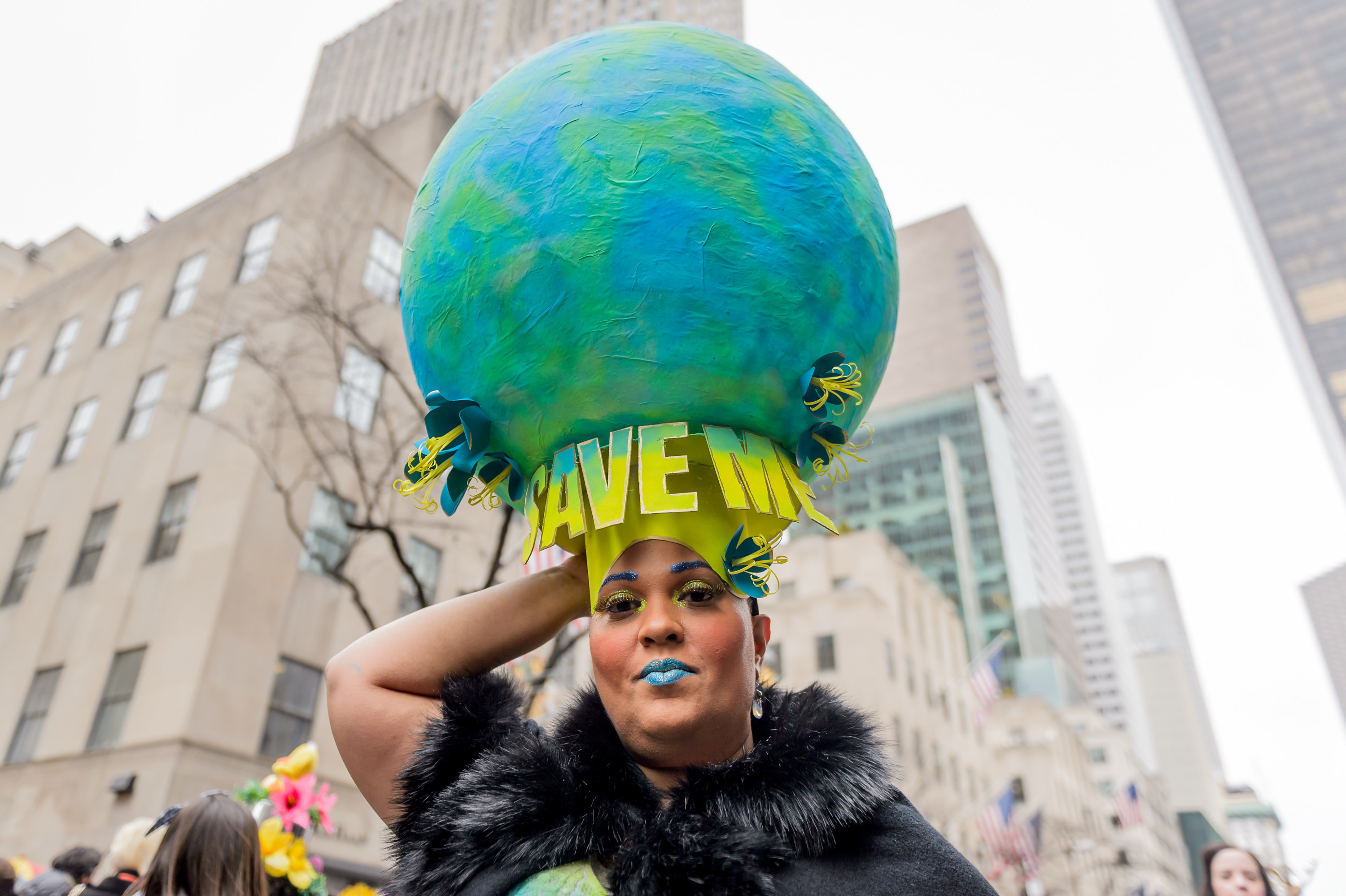 A woman with a hat that looks like a globe and says Save Me