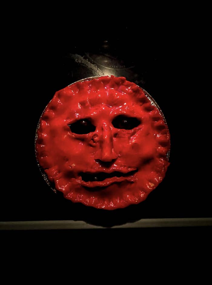 A cherry pie with a scary face molded into it against a dark background