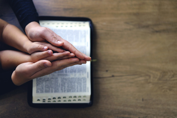Two pairs of hands praying together over a Bible.