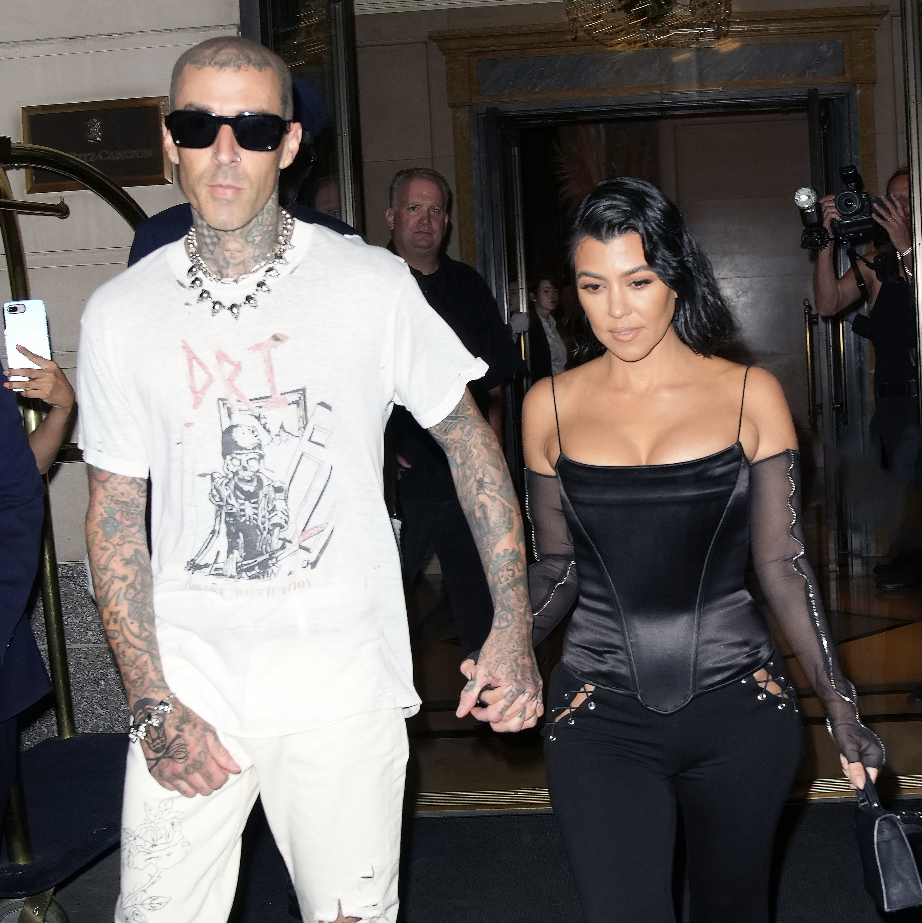 Travis holds Kourtney&#x27;s hand while walking out of a building
