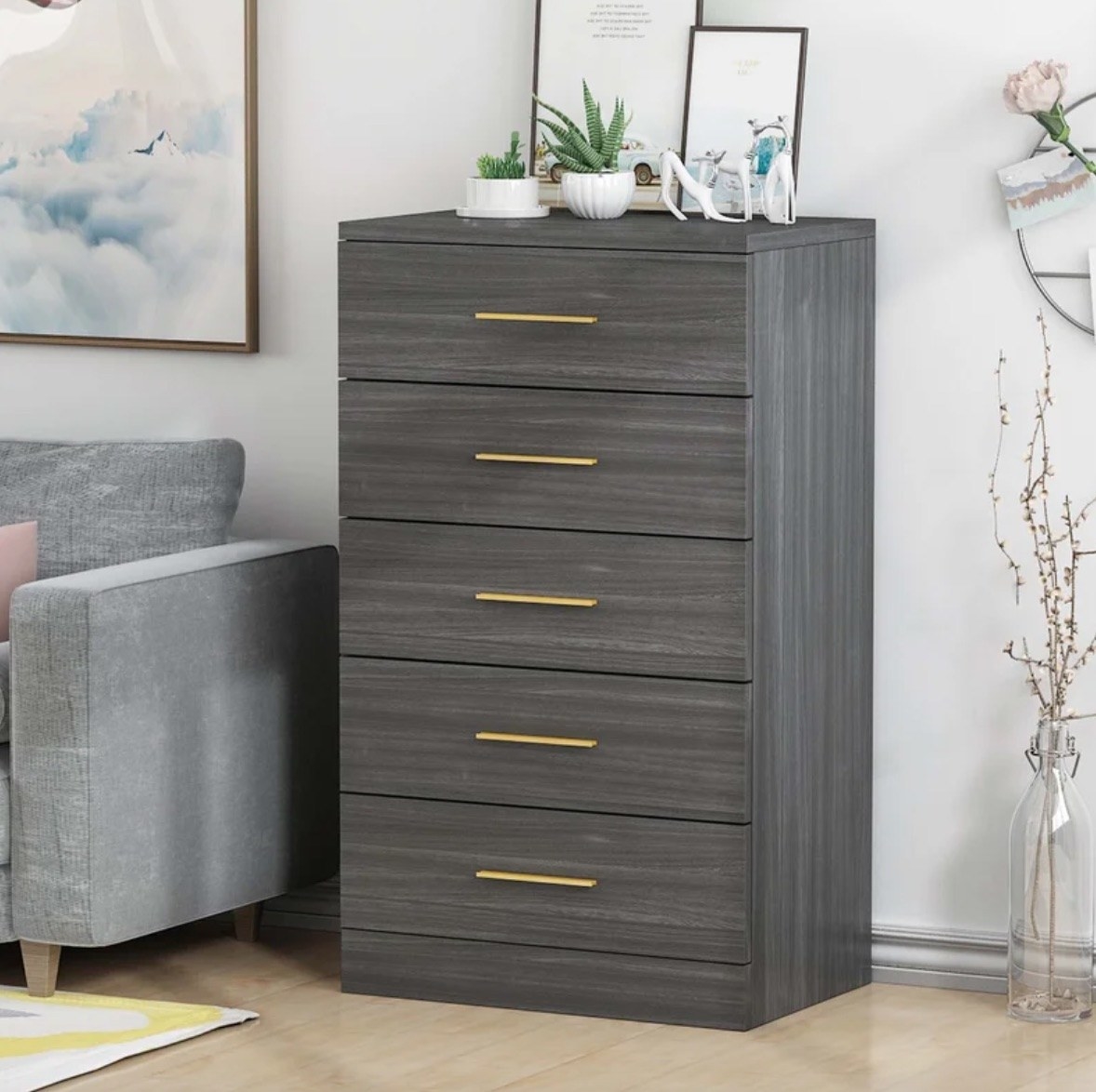 a tall charcoal chest of drawers with gold pulls in a living room, with plants and decor on top