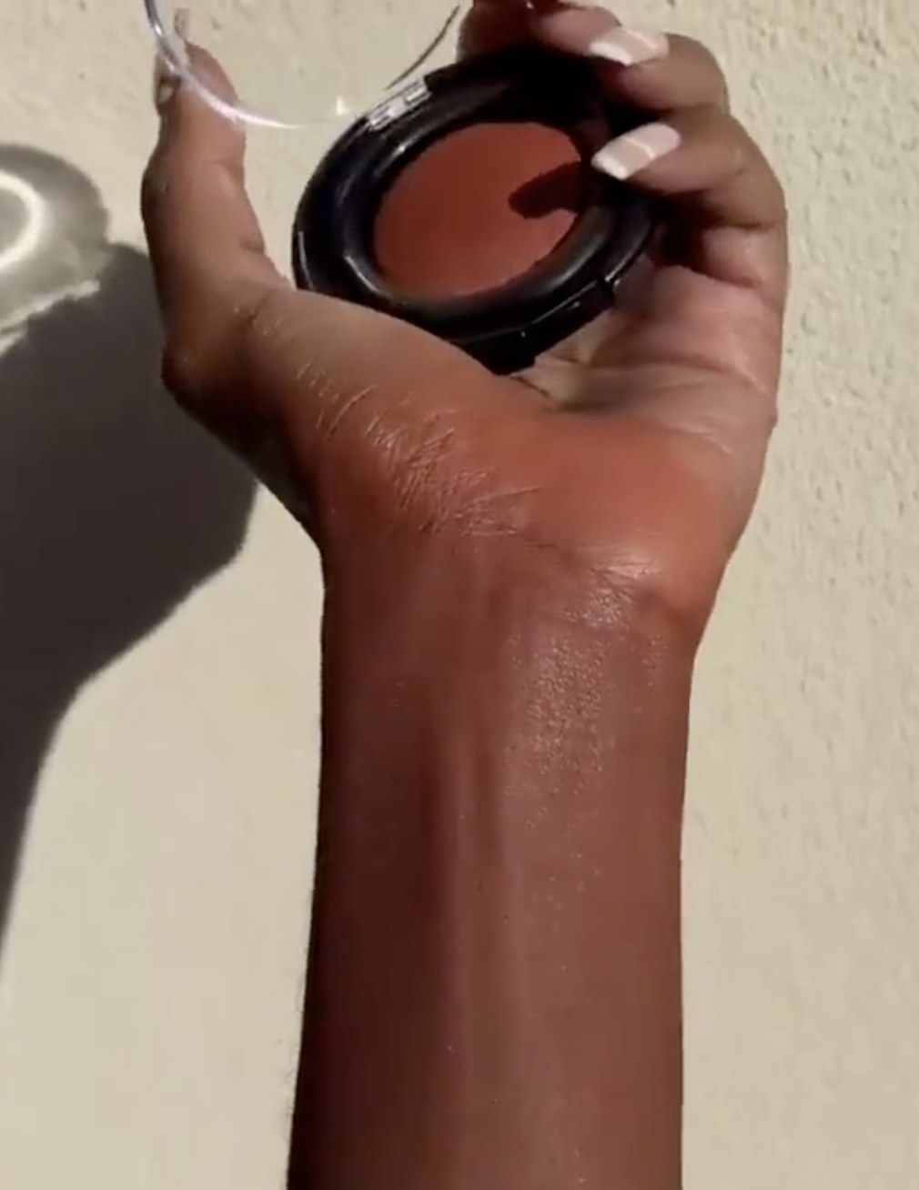 a person holding their blush with a swatch of the blush on their wrist