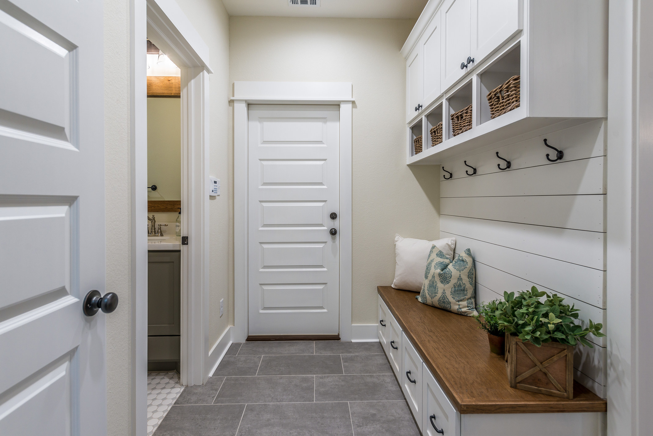a mudroom with wooden panels, hooks, and long bench