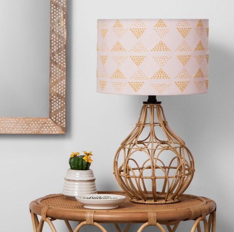 A rattan table lamp with a pink shade