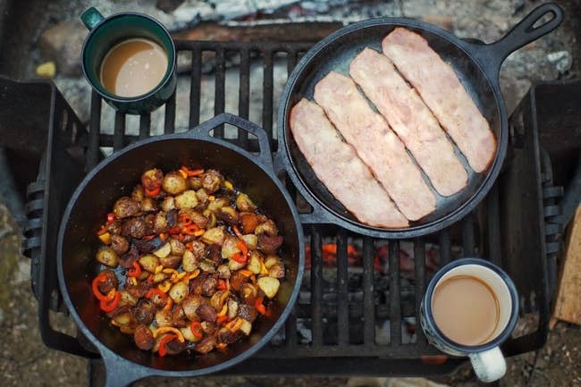 two cast iron skillets cooking food on a camp fire