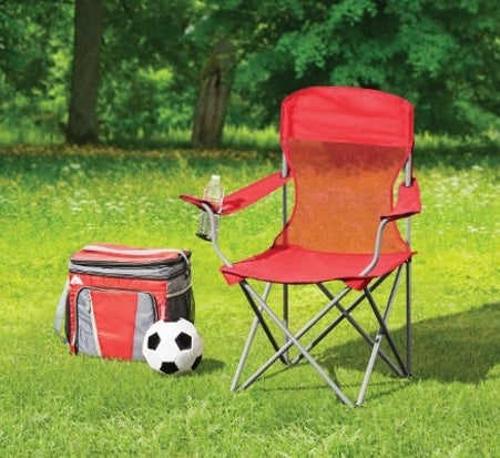 red camping chair with a cup holder next to a soccer ball and cooler