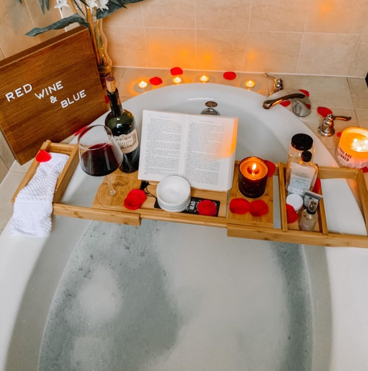 Reviewer image of a wooden bath caddy holding an book, wine glass, wine bottle, candle, and more accessories