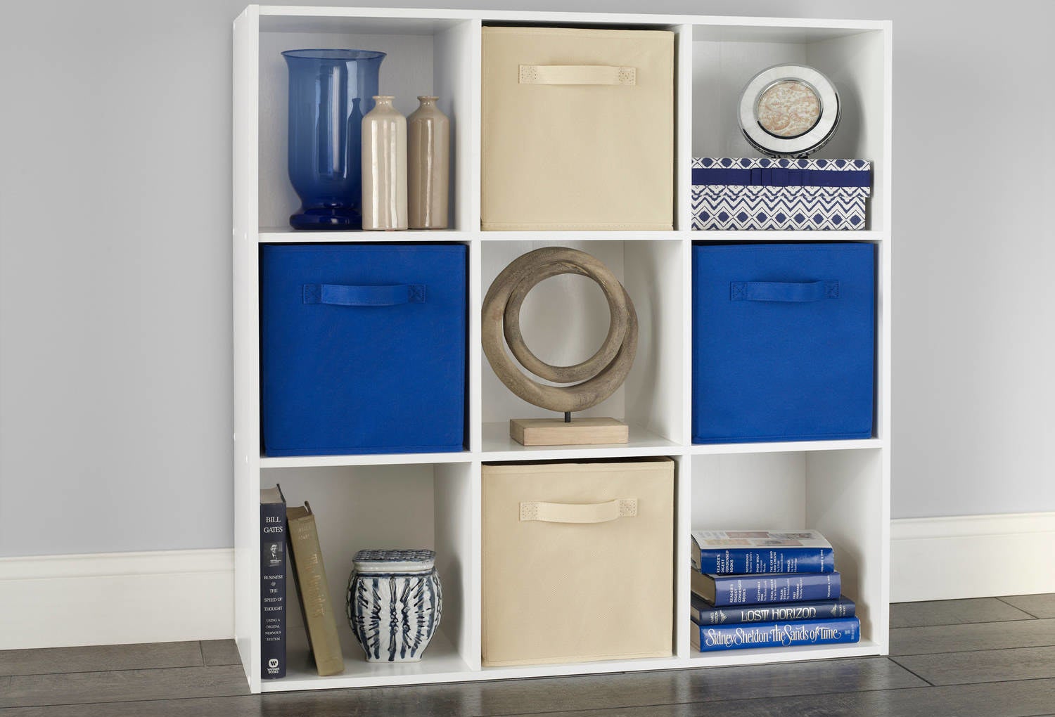 An image of a white nine-shelf organizer used to hold books, vases, and fabric storage bins