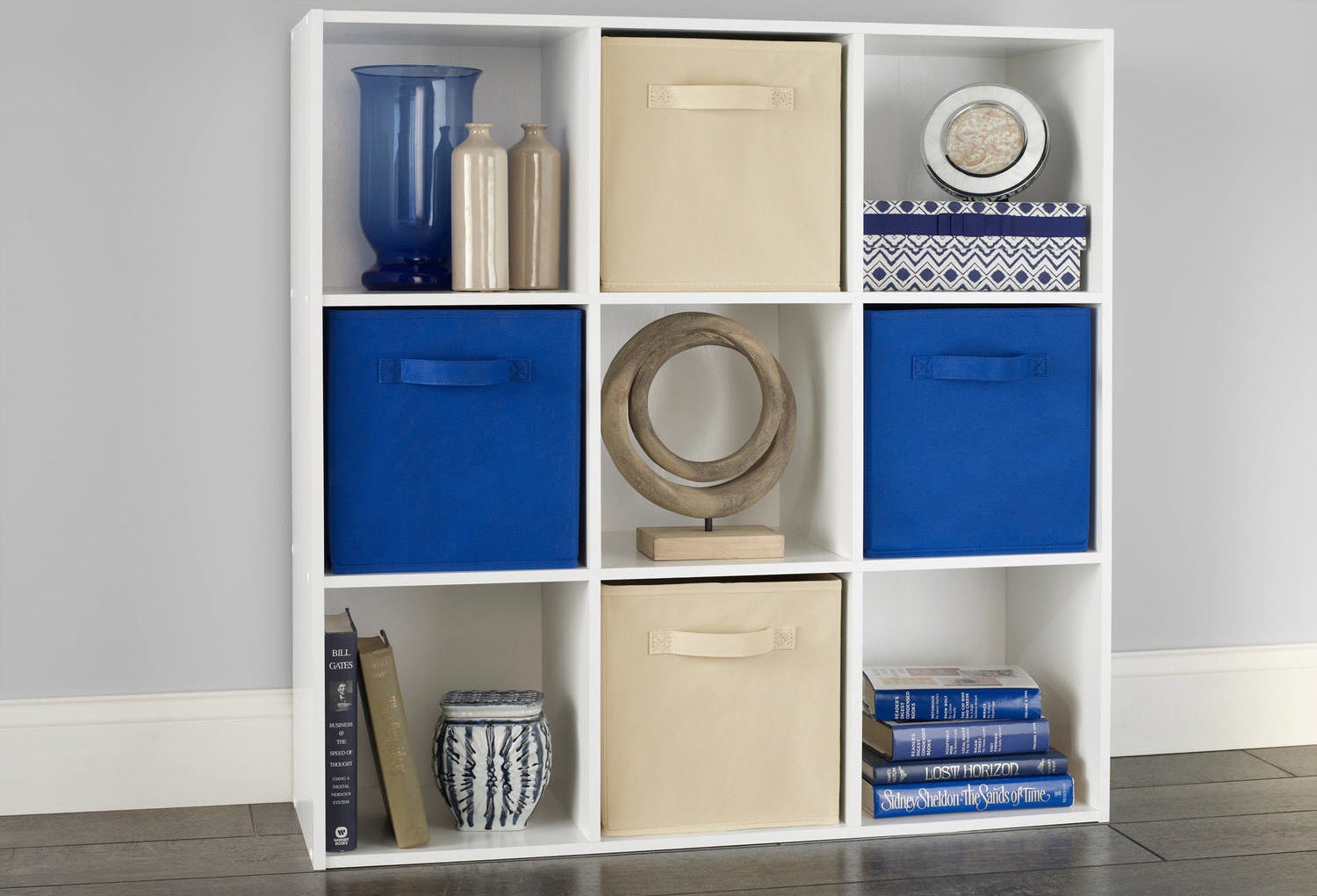 An image of a white nine-shelf organizer used to hold books, vases, and fabric storage bins