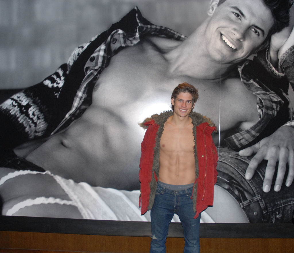 a shirtless store model stands in front of the entrance poster