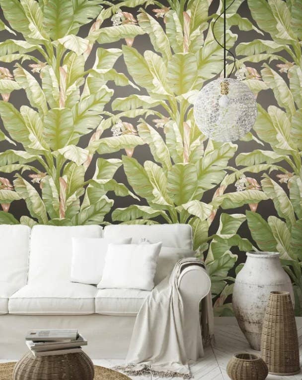 Banana leaf wallpaper on black background behind a white sofa and rattan furniture. 