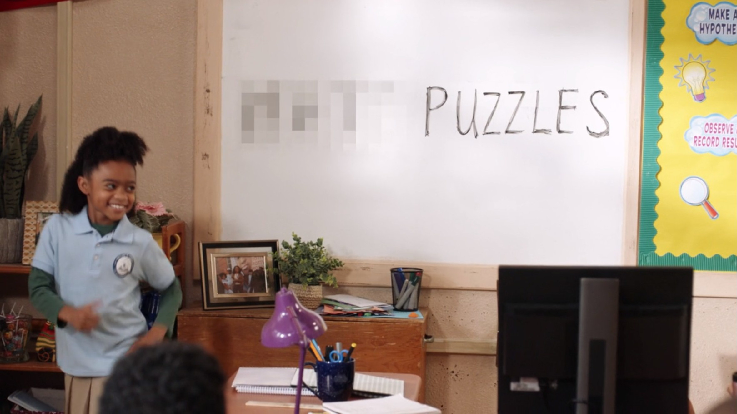 A young student is smiling as she dances next to a white board that reads &quot;[BLEEP] PUZZLES&quot;