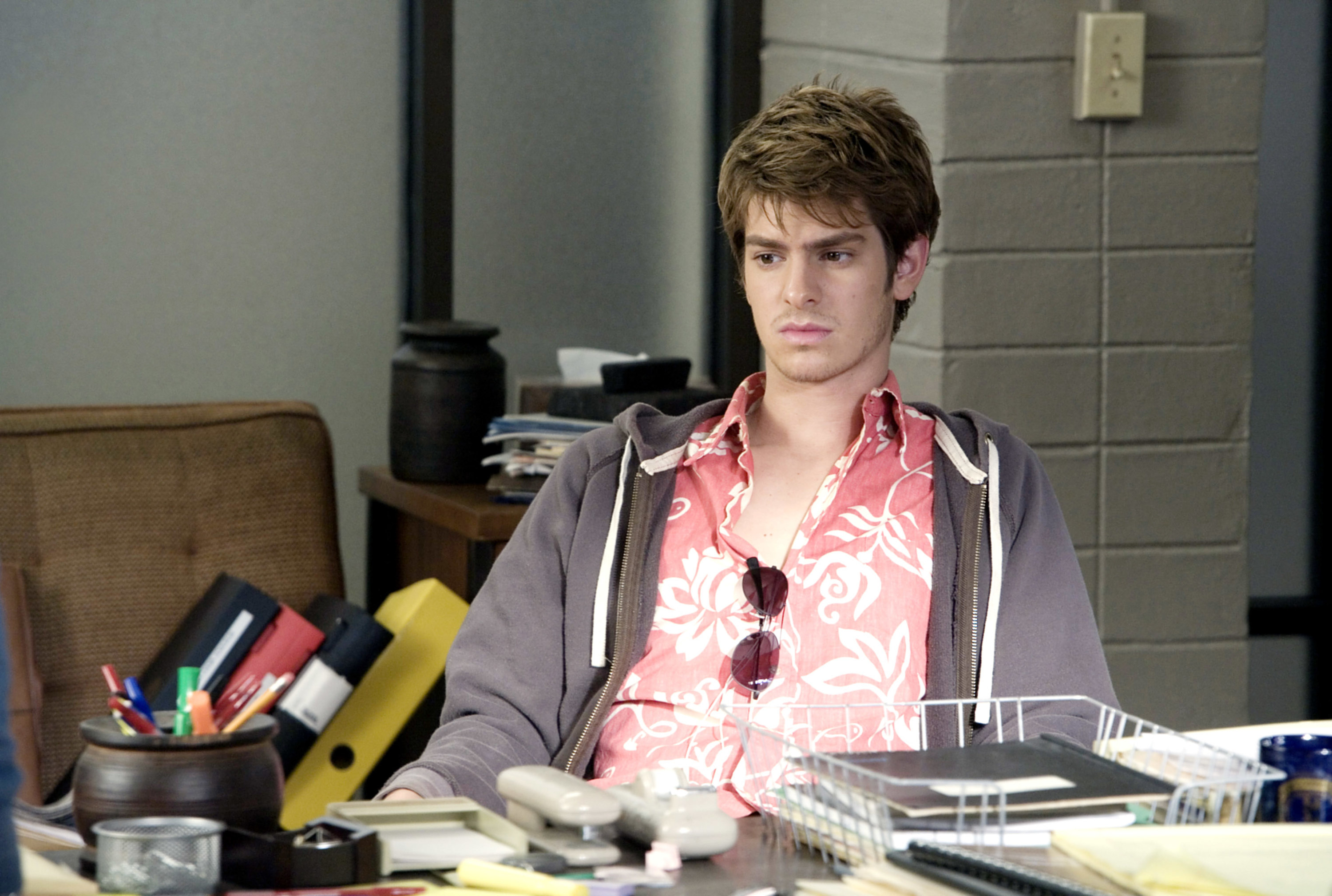 Andrew Garfield sits at a desk
