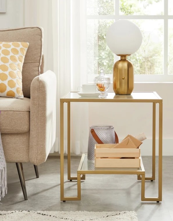 Glass side table with gold frame placed next to a couch.