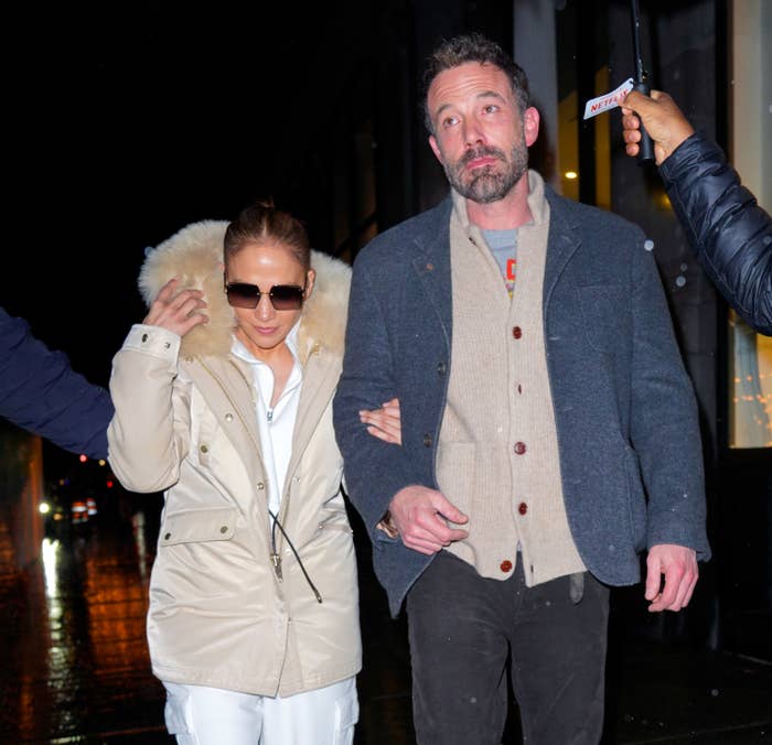 Ben and Jennifer walk down the street under an umbrella