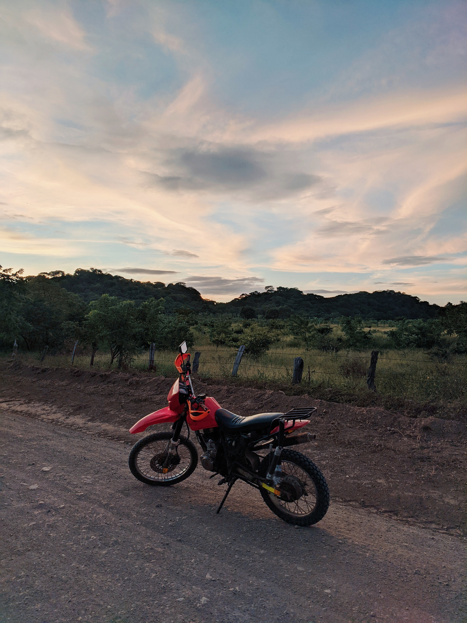 A motorcycle sits on a rural dirt road.