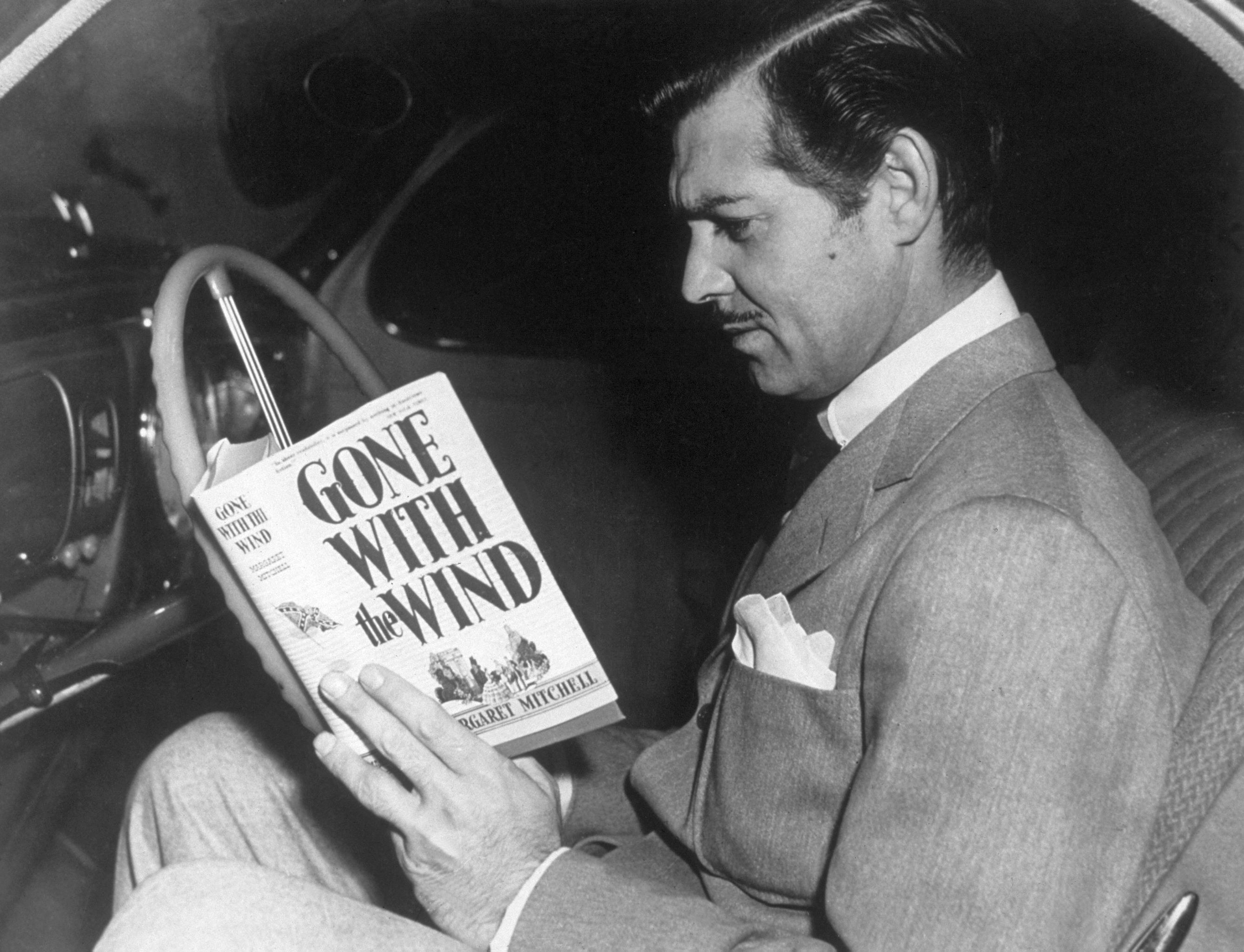 Clarke Gable reads Gone With the Wind in the driver&#x27;s seat of a car