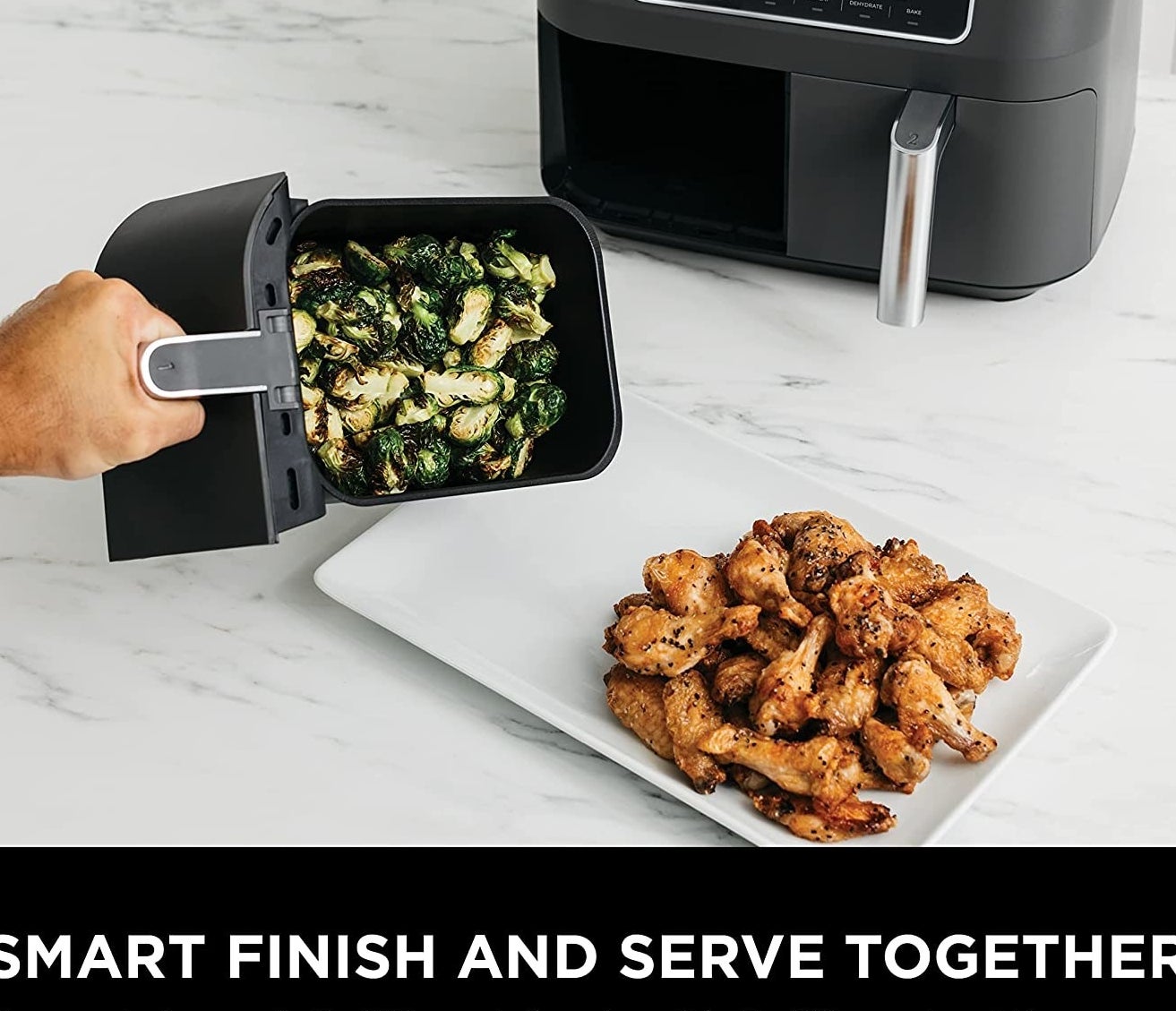 Someone plating up some vegetables from one of the fryer baskets onto a plate of chicken wings, with the Ninja fryer behind it