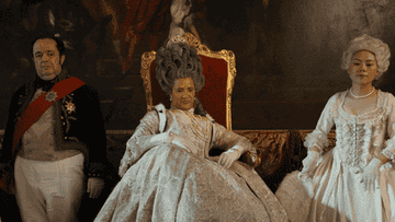 Queen Charlotte waves someone away while sitting on her throne
