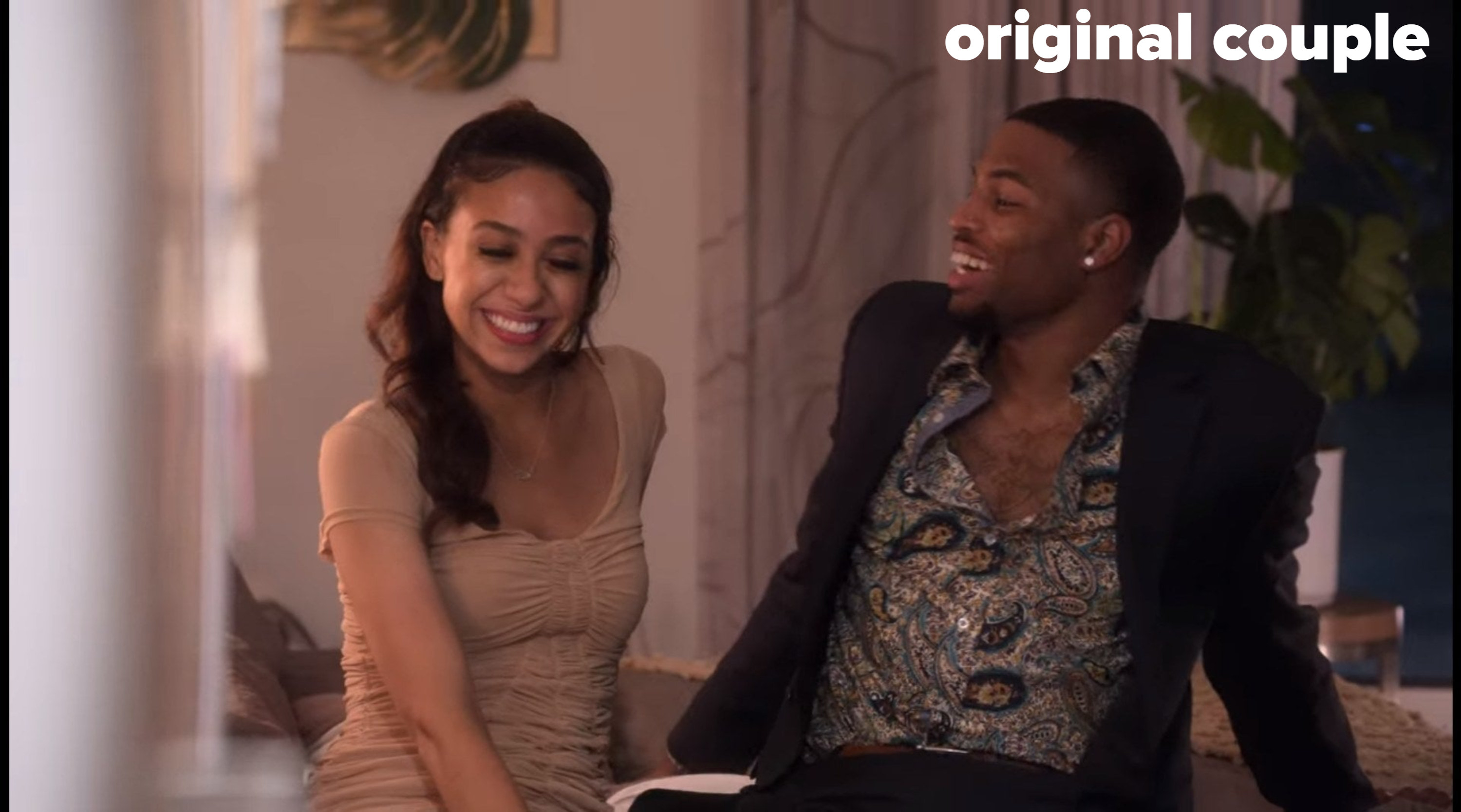 Rae and Zay sit on a bed, laughing together