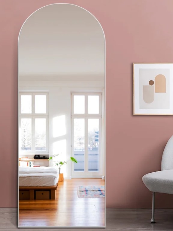 Arched-top wall mirror leaned against a blush colored wall.