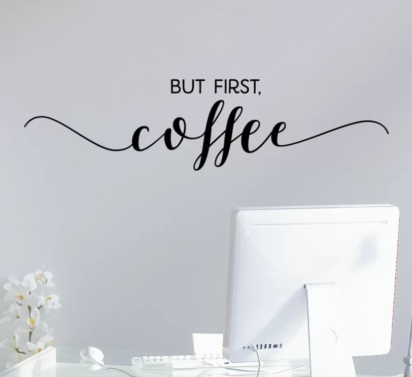 Black wall decal that reads &quot;But first, coffee&quot; on gray wall in an office room.