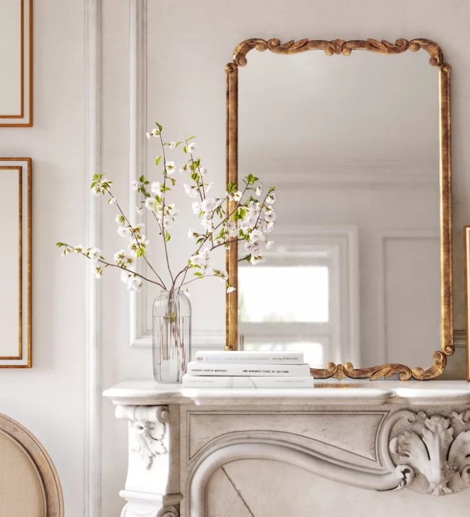 Mirror with gold contemporary frame sitting on top of a stone mantel. 