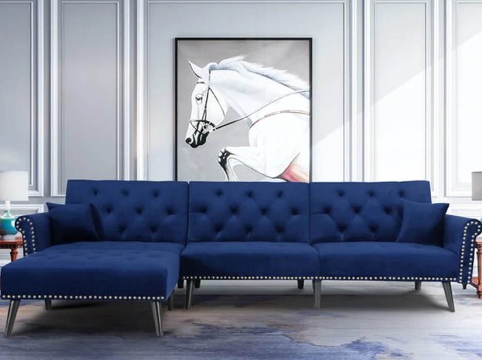 Blue velvet corner sofa with tufted cushions and silver studs on the arms. 
