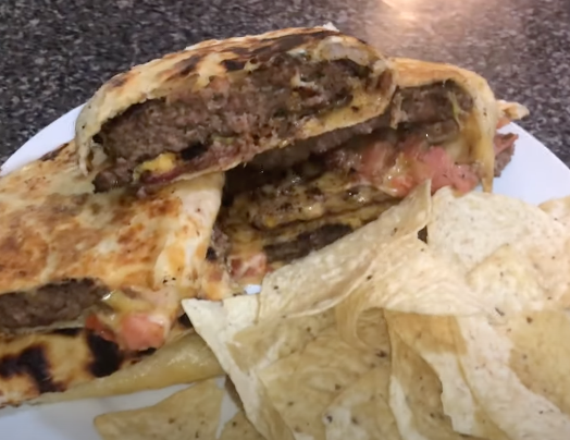 A hamburger in a tortilla with some tortilla chips on a plate