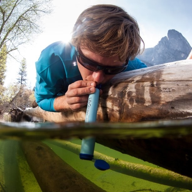 A model drinking from a lake using the life straw outdoors